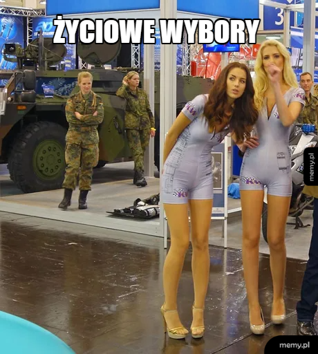 Dwie kobiety w obcisłych strojach na tle wojskowego pojazdu.