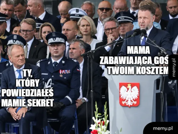 Mężczyzna w garniturze siedzi obok mundurowego, obaj na tle tłumu.