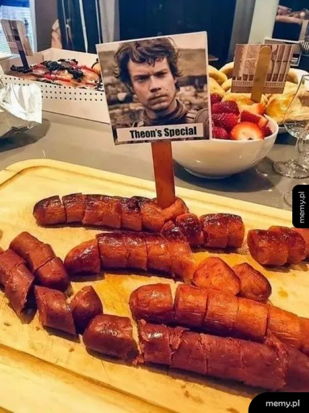 Deska z pokrojonymi kiełbaskami, z napisem 'Theon's Special' i zdjęciem mężczyzny.