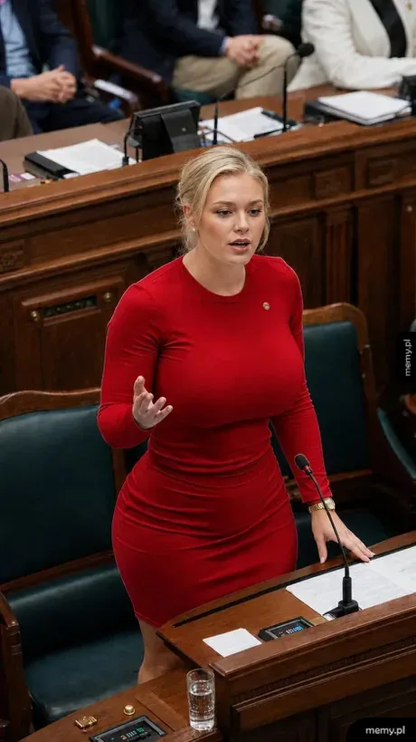 Kobieta w czerwonej sukience przemawia w parlamencie.