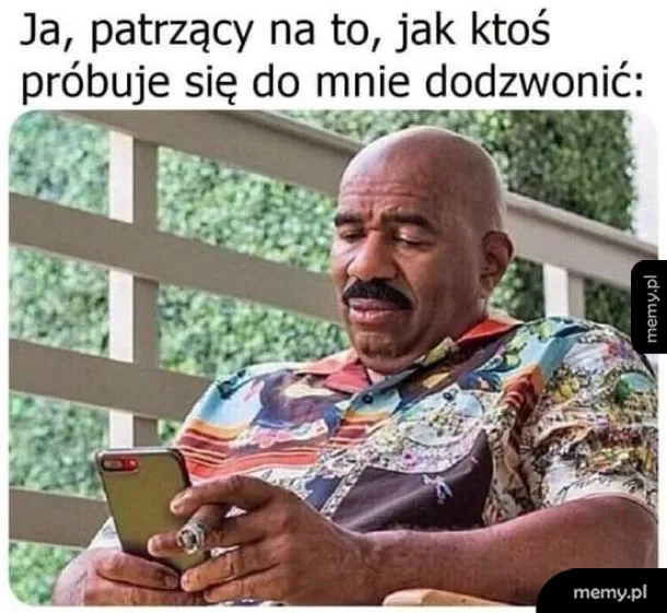 Steve Harvey w kolorowej koszuli patrzy zniecierpliwiony na telefon.